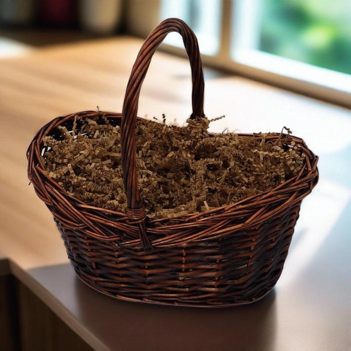 Woven gift basket with tall handle, lined with brown shredded filler on a tabletop