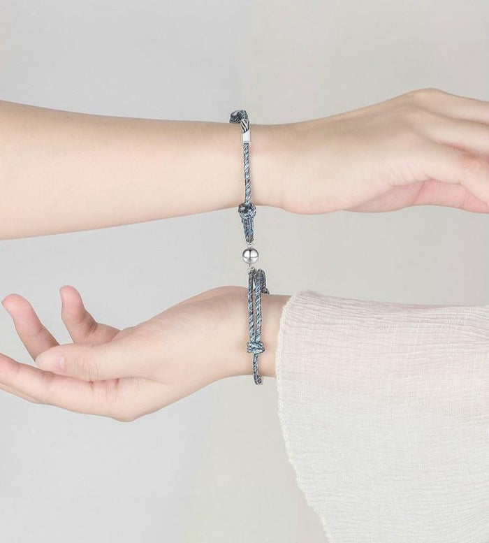 Braided grey couple attraction bracelets on wrists with metal beads and charm pendants