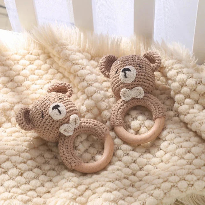 Two crochet teddy bear teethers with wooden rings on a textured cream rug