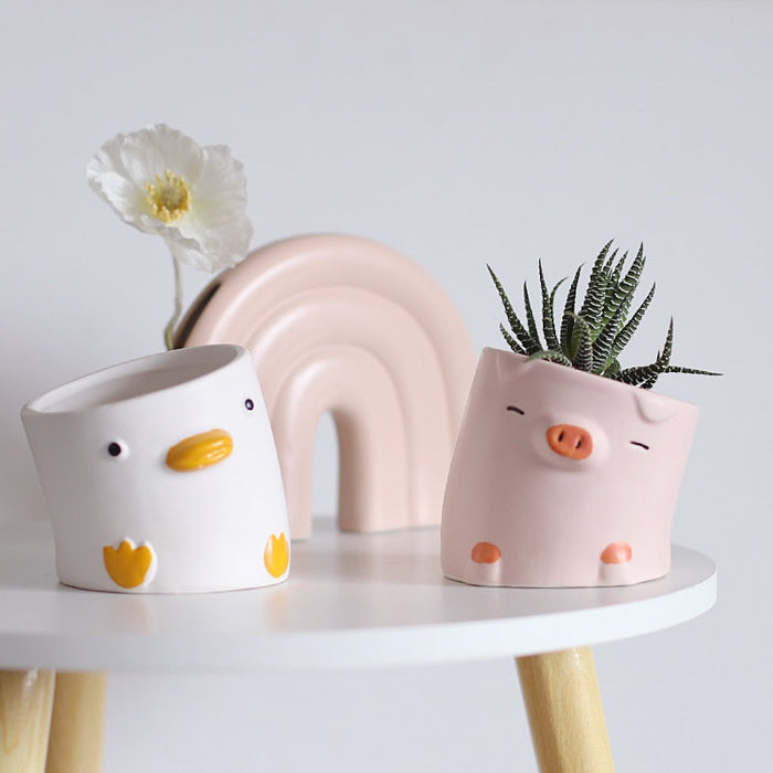 Pair of animal ceramic planters: white duck and pink pig with small plants.
