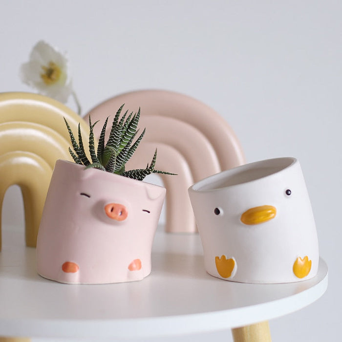Pink pig and white duck ceramic planters on shelf, with a pastel arch planter behind.