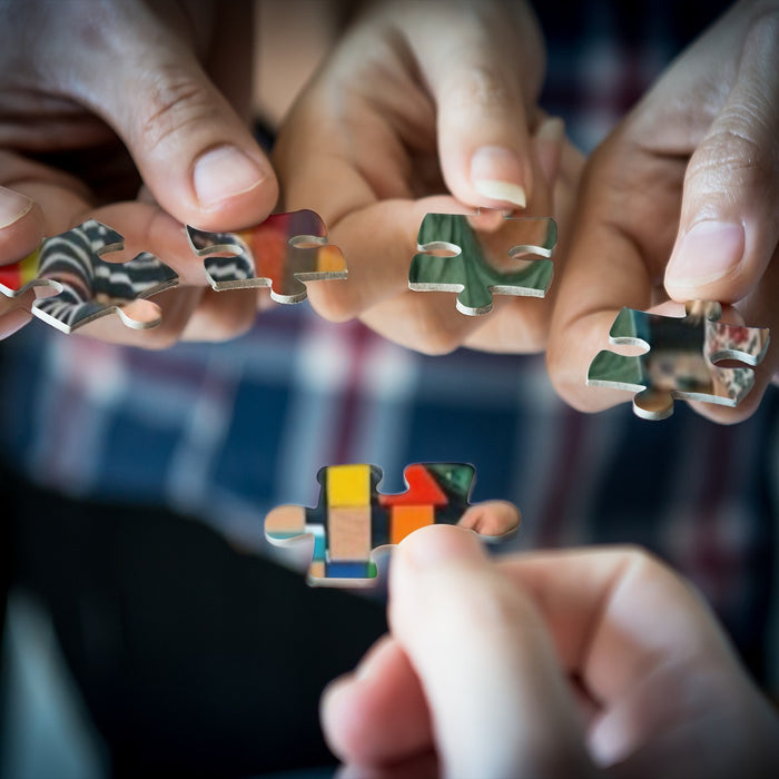 Hands holding small wooden jigsaw pieces, fitting colorful shapes together
