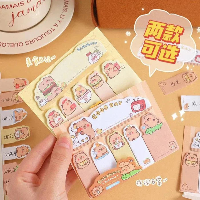 Capybara bookmark sticky notes set with pastel tabs and cartoon faces, held in hand