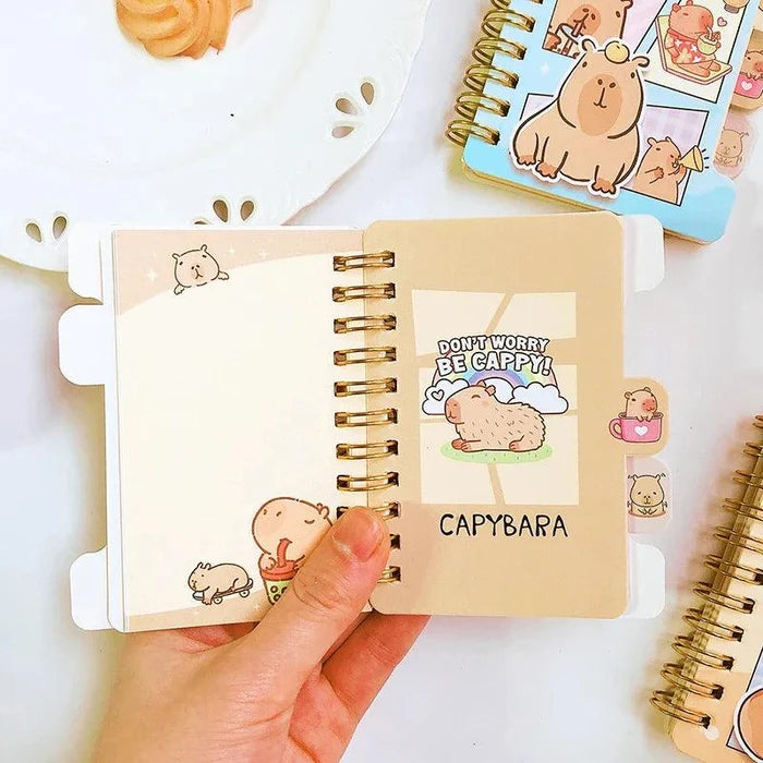 Mini notebook open flat with capybara cover art and spiral rings, beige cover