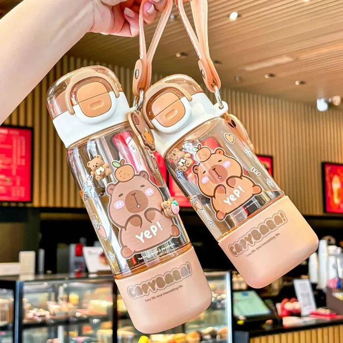 Pair of clear water bottles with peach lids and capybara graphics, shown in hand