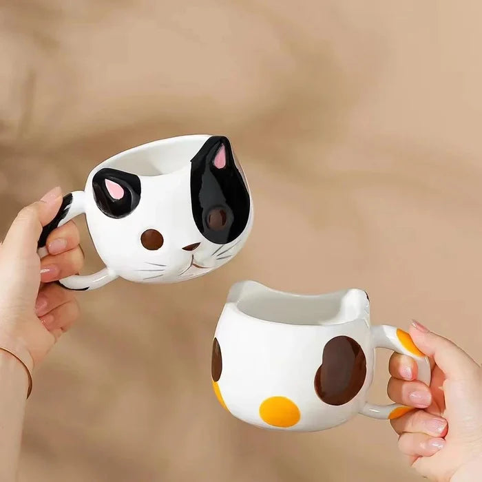 Cat ceramic mug with white body, black ear spots and yellow dot, held in hands