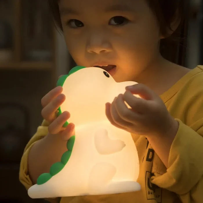Dinosaur night light glowing as a child holds it with both hands, green tail accents