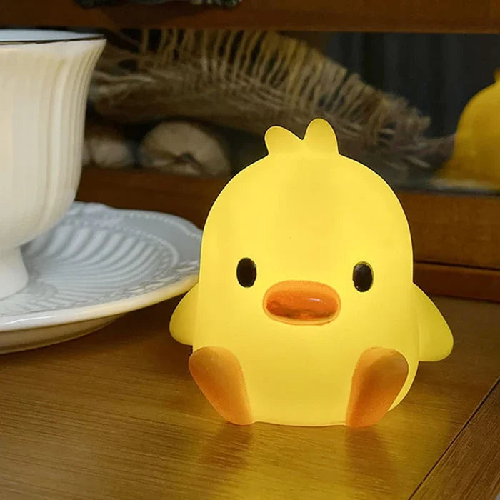 Yellow duck-shaped night light with orange beak and black eyes on wooden surface