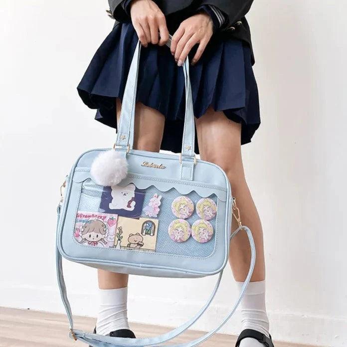Light blue Ita messenger bag with character collage window, scalloped flap, pom-pom charm