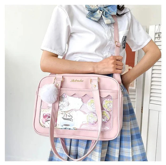 Pink Ita messenger bag with scalloped top, character collage window, pom-pom charm