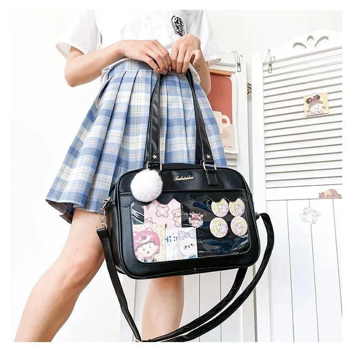 Black Ita messenger bag with scalloped flap and character collage window, pom-pom charm