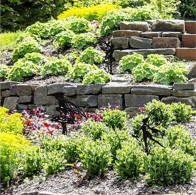 Black fairy silhouette garden stakes on slender spikes beside garden plants and stones