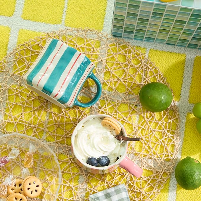 Straw-covered table setting with striped ceramic mugs and curved handles