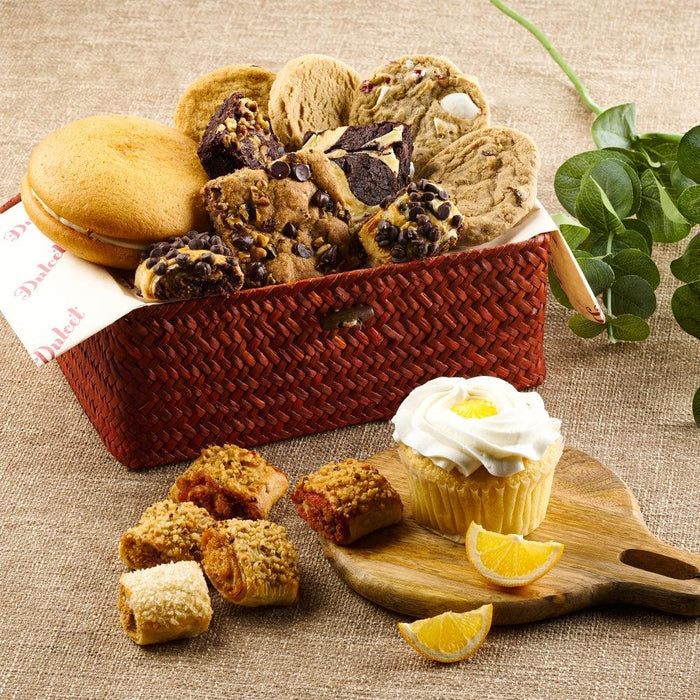 Red woven wicker basket filled with cookies, macarons, and a frosted cupcake