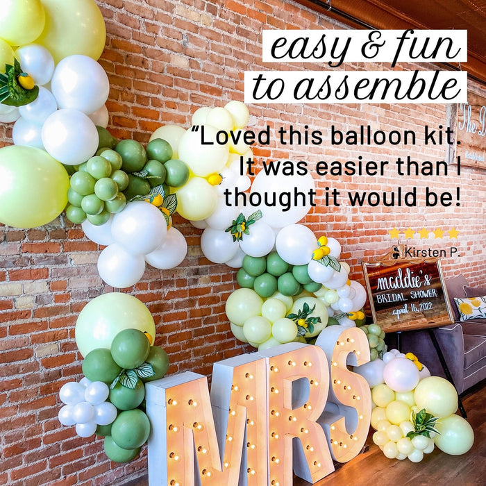 Balloon garland kit with green, white, and pale yellow balloon clusters and letter balloons