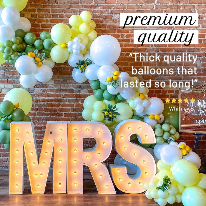 Balloon garland kit with green, white, and pale yellow balloons around lit letter balloons