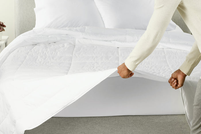 A person spreading the Down Alt Duvet over a bed