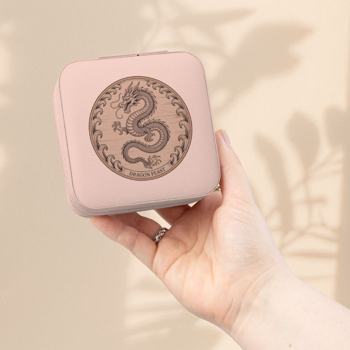 Compact jewelry travel case in light pink with dragon emblem, held in hand.