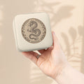 Compact jewelry travel case in ivory with dragon emblem, held in hand.