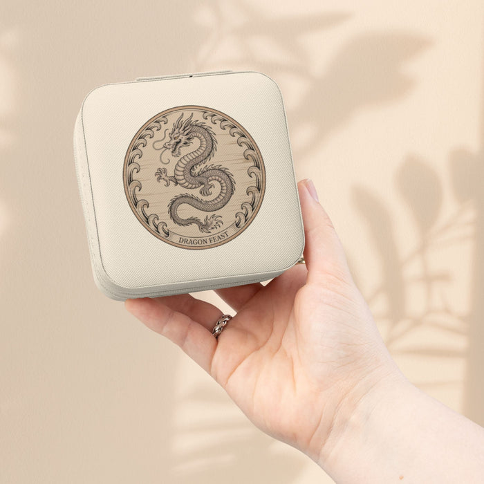 Compact jewelry travel case in ivory with dragon emblem, held in hand.