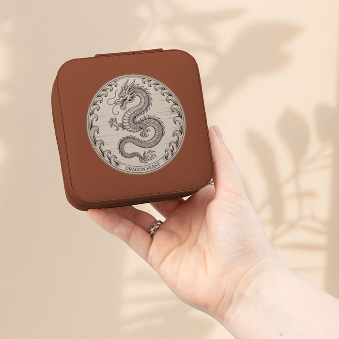 Compact jewelry travel case in brown with dragon emblem, held in hand.