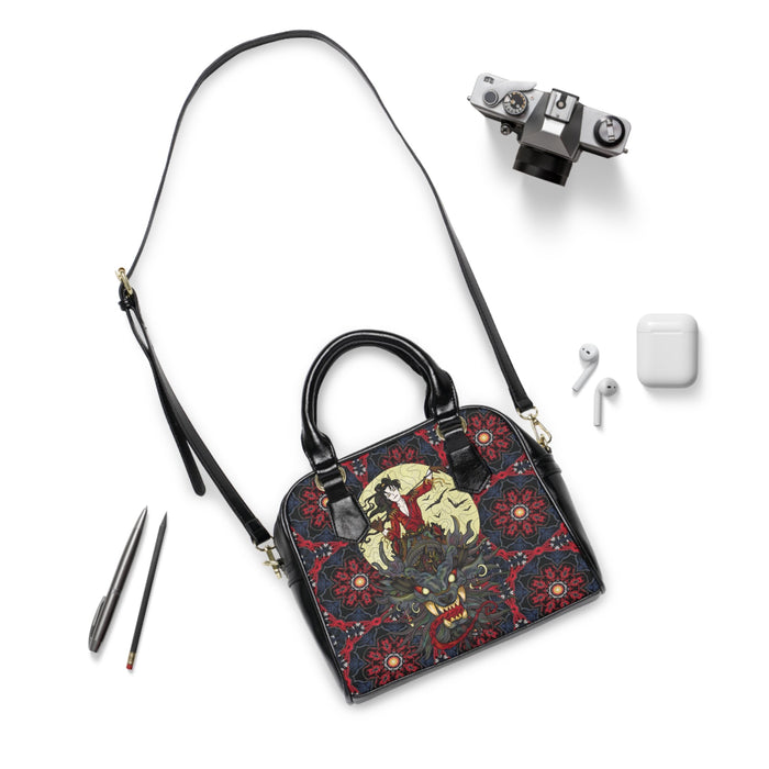 Black handbag with long crossbody strap, front graphic panel, and gold-tone hardware