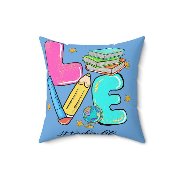 Square faux suede pillow, light blue print showing pink teacher, pencil, stacked books, globe and teal 3