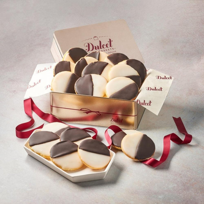 Black and white cookie tin with assorted cookies and red ribbon, open on tray