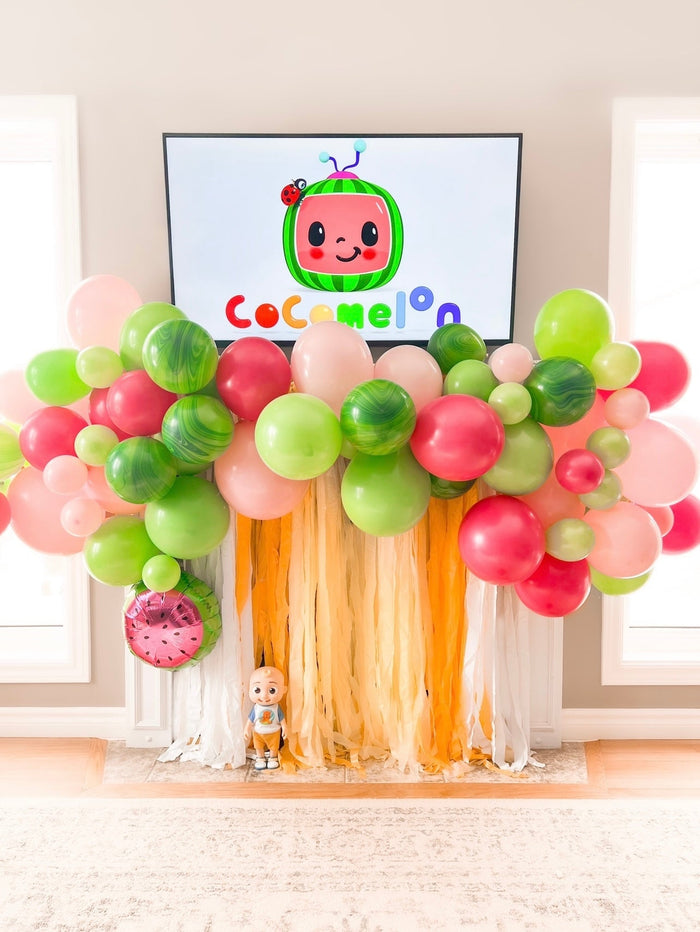 Fruit-themed balloon garland with pink, lime green, and peach balloons in a festive arch