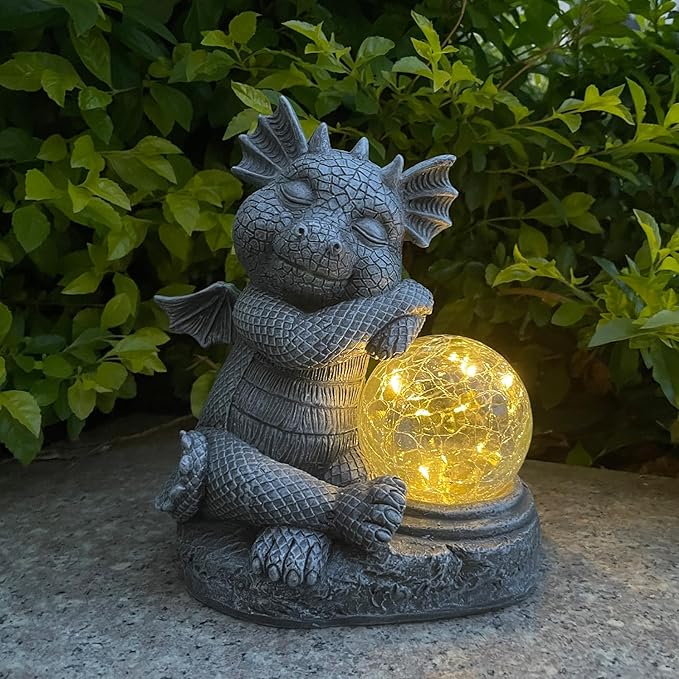 Blue-gray dragon resin figurine holding a glowing glass orb in its arms, outdoor statue