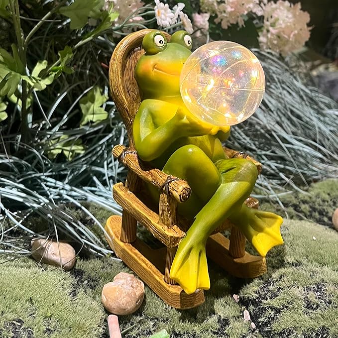 Frog garden statue with glowing bubble light on wooden rocker, surrounded by rocks