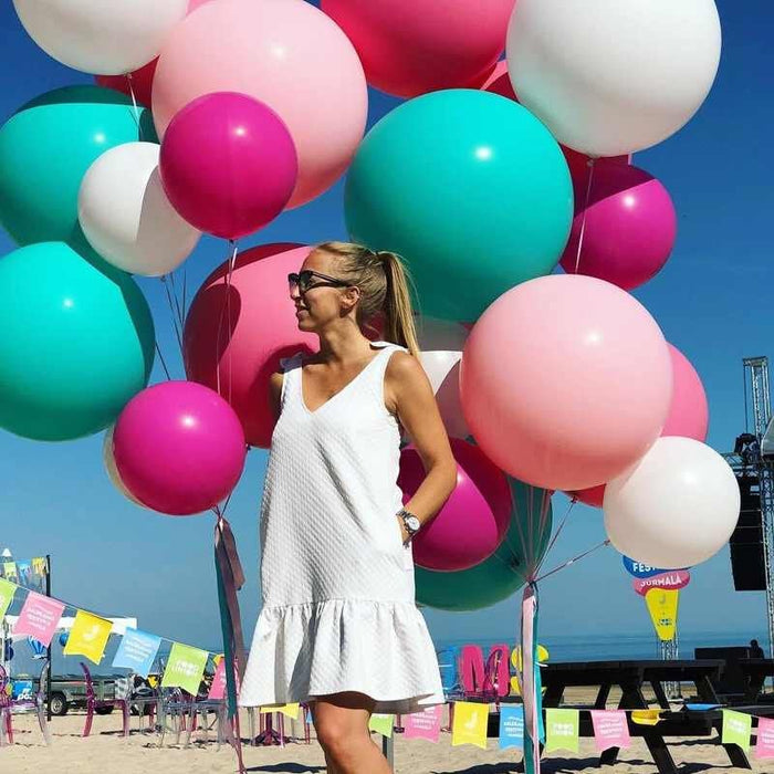 Large cluster of teal, pink, magenta, white, and green balloons outdoors.