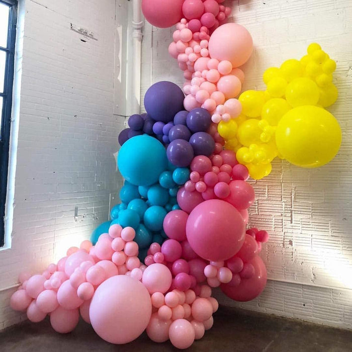 Balloon arch with large pink, purple, blue, and yellow balloons indoors.