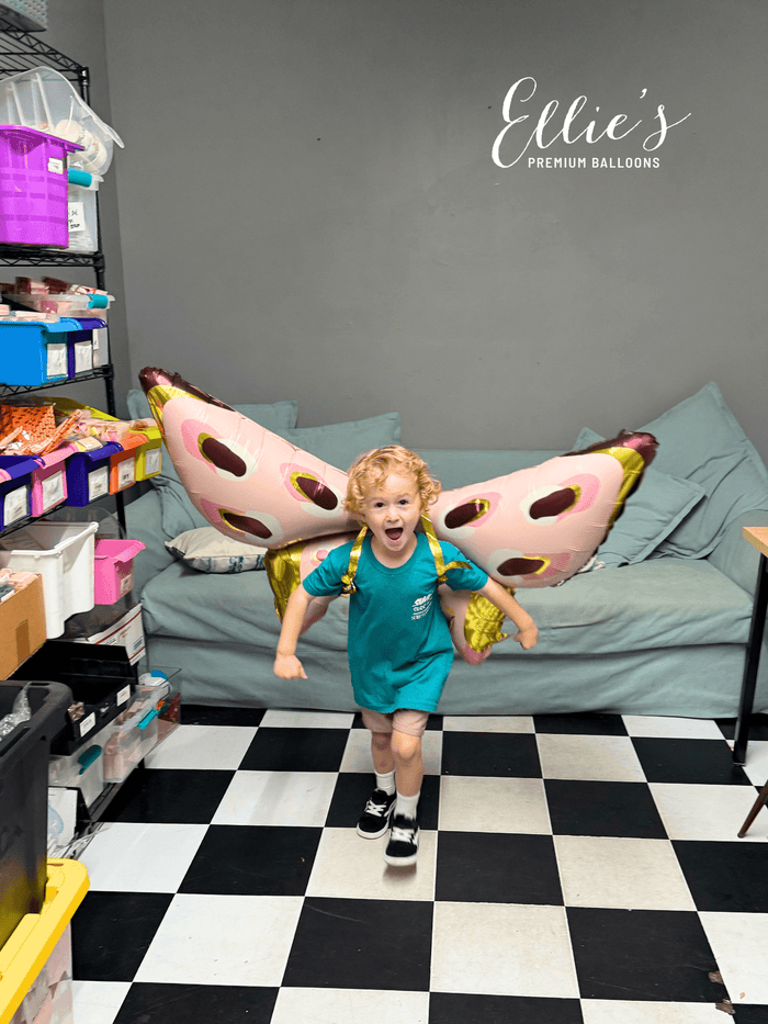 Pink butterfly foil balloon with gold center and oval spots, held indoors.