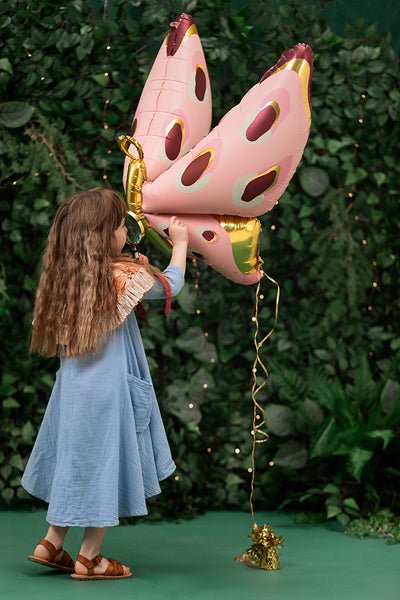 Pink butterfly foil balloon with gold center and oval spots, held by person.