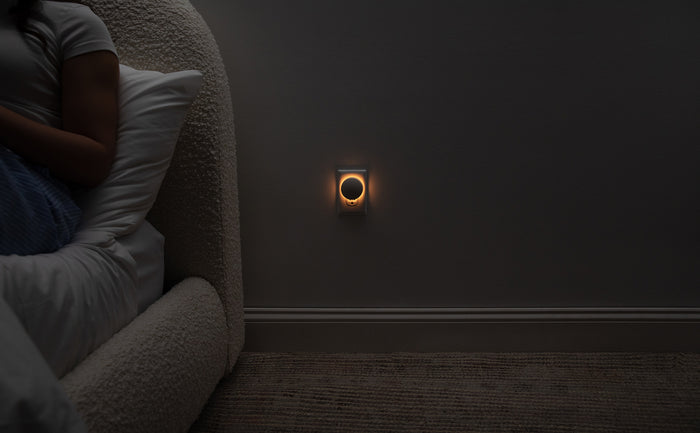 Image of the Glow Nightlight turned on next to a bed, emitting a soft, orange glow.