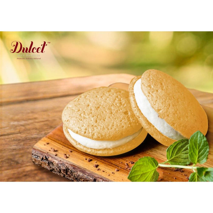Two round bakery cookies with white filling on a wooden board, mint leaves.