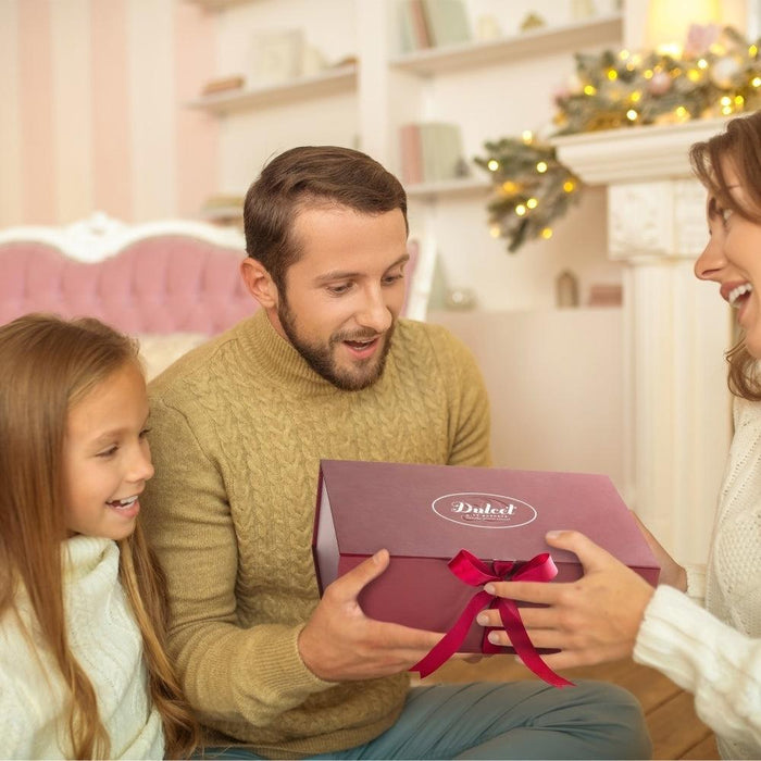 Family holding a burgundy-ribbon bakery gift box at home, smiles and laughter.