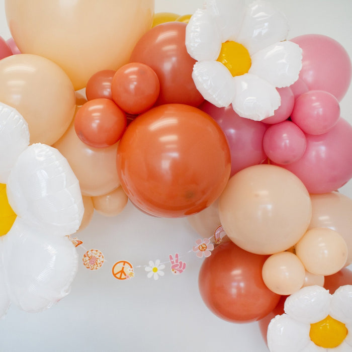 Close-up balloon cluster with orange and pink balloons and a white daisy centerpiece