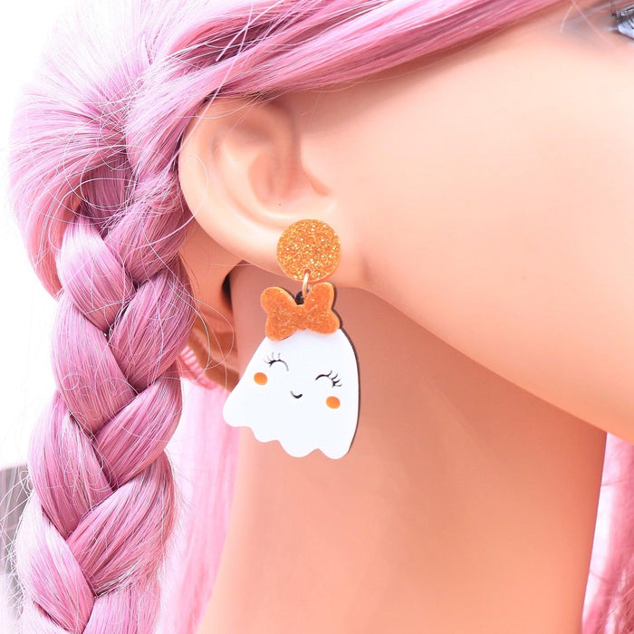 Ghost face drop earrings in orange glitter with white face, worn with pink braided hair