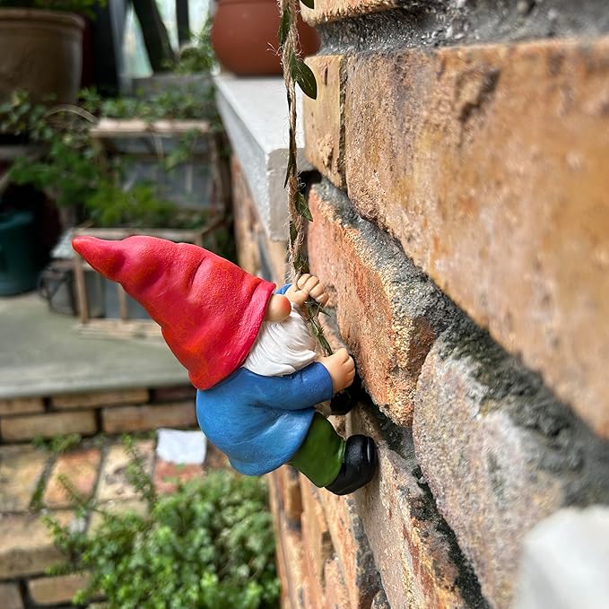 Climbing gnome statue holding rope on stone wall, red hat, white beard, blue body, green pants
