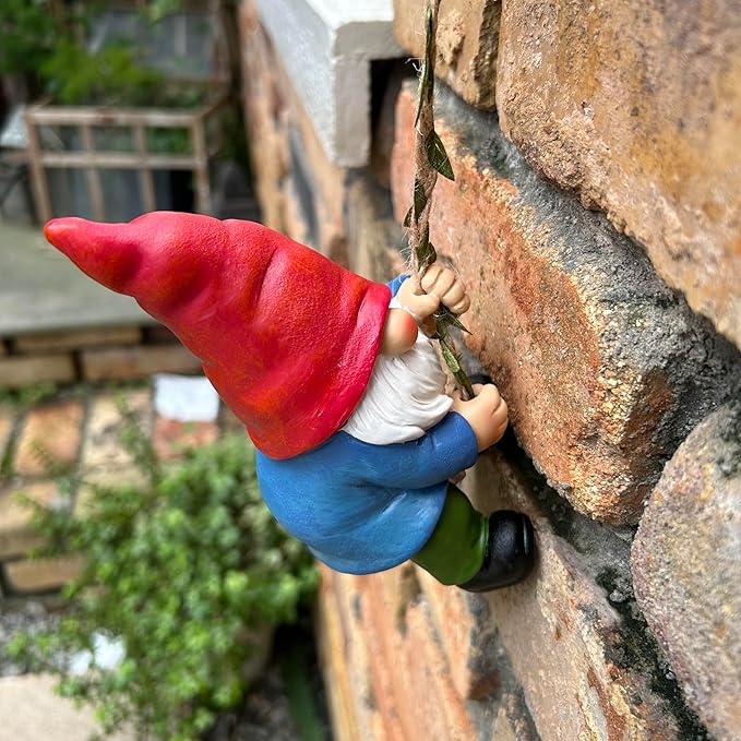 Climbing gnome figurine on rope against stone, red hat, white beard, blue body, green pants