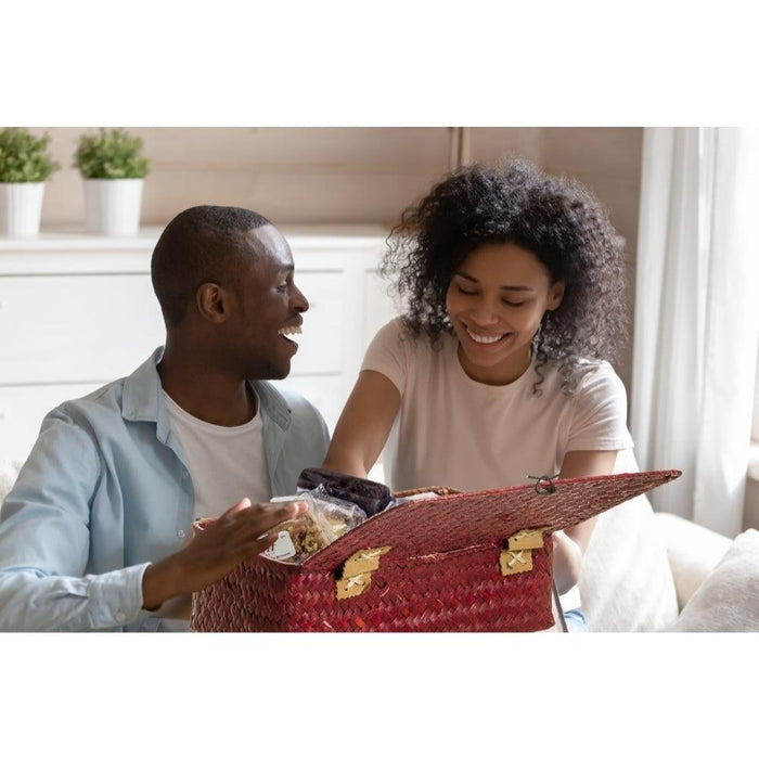 Red woven wicker gift basket held by people indoors, with handle and open top