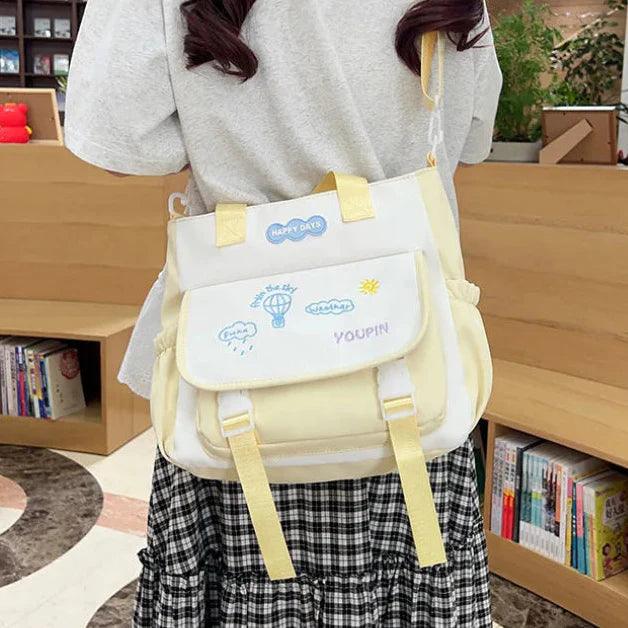 Cream tote bag with front flap pocket, adjustable straps, and small logo patch.