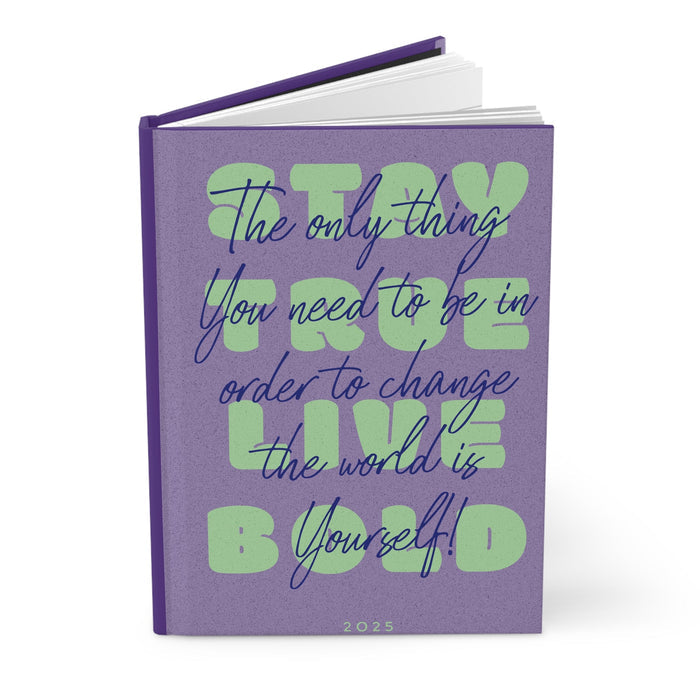 Hardcover journal with purple cover and green inspirational lettering; stacked pages visible.