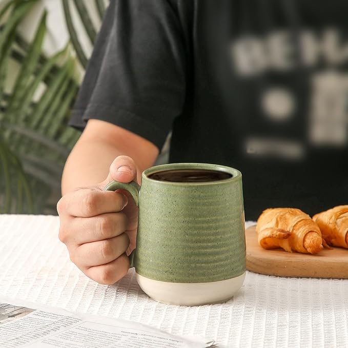 Green ceramic coffee mug with curved handle and speckled glaze, held by hand