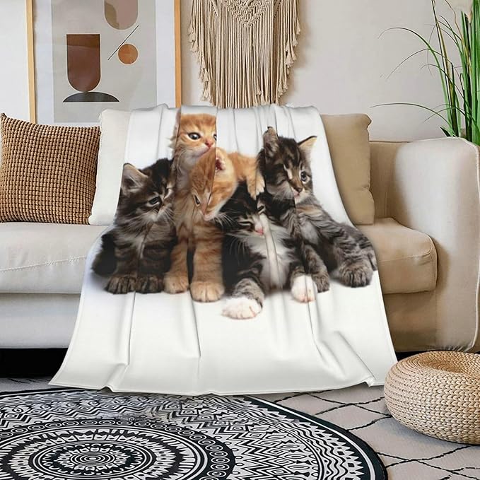 Cats throw blanket draped over a couch cushion, featuring a group of kittens on white fleece