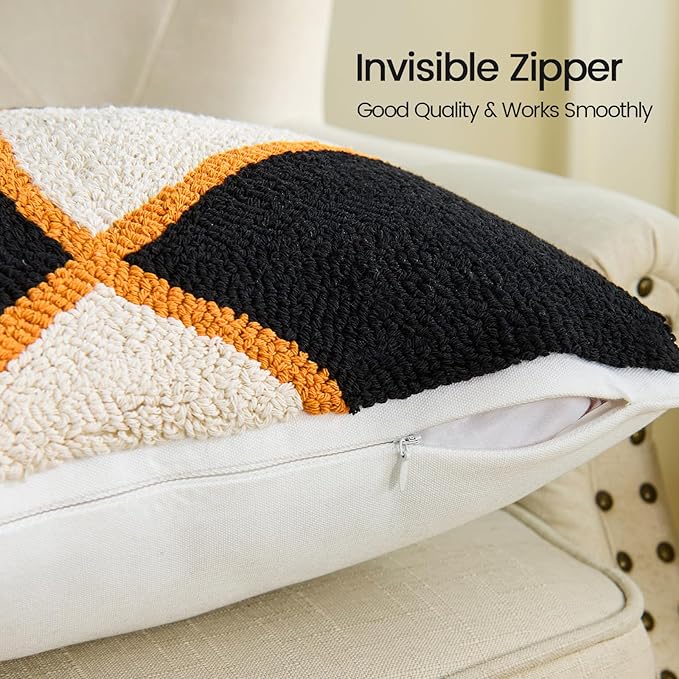 Square tufted pillow cover with black face, tan cross, and orange edging; seam visible