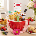 Red ceramic mug gift basket with baking mix, syrup, and assorted breakfast items