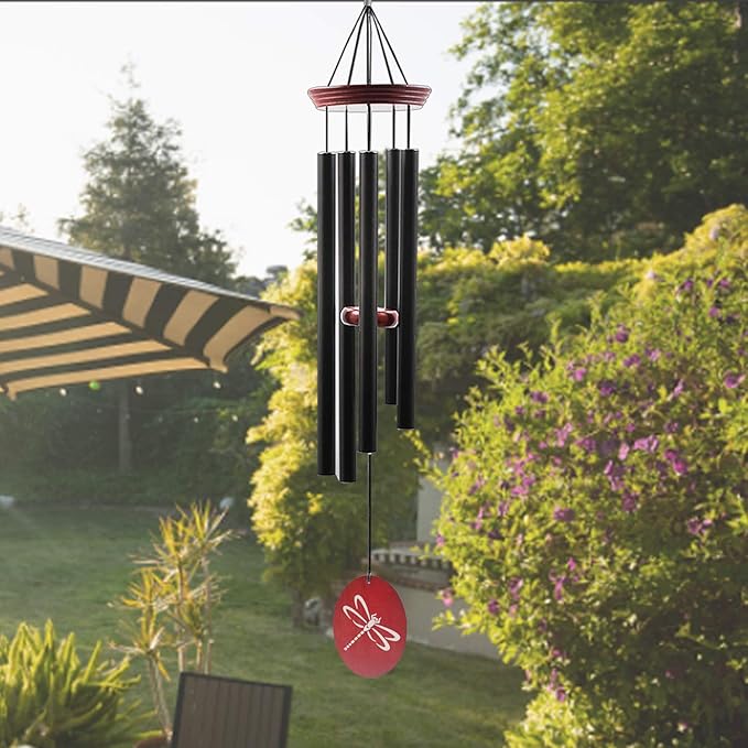 Outdoor wind chime with black tubes and red dragonfly disc, suspended in garden.